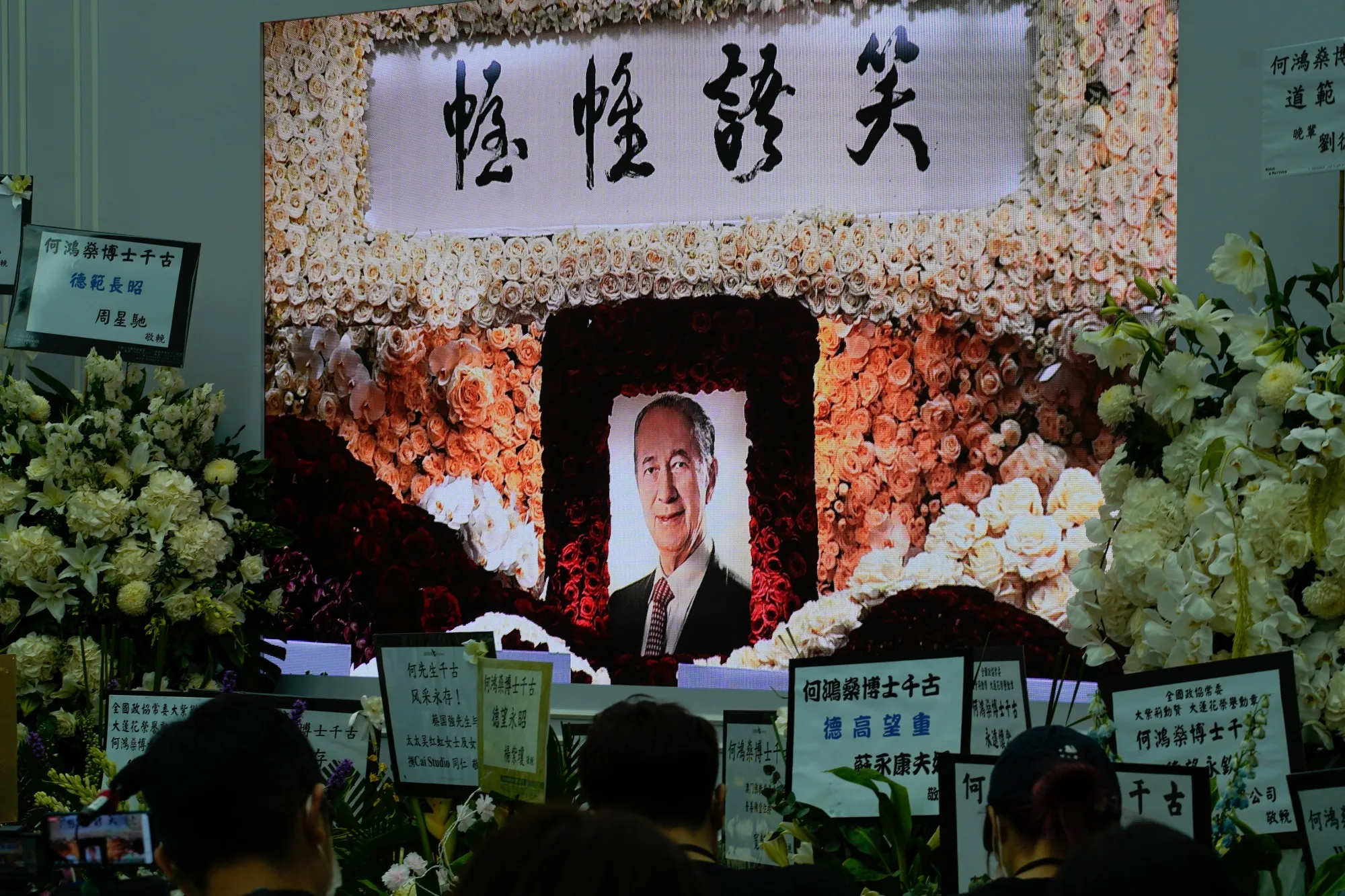 Members of the media sit in front of a portrait of Stanley Ho displayed alongside floral wreaths in the media room at his funeral in Hong Kong, on July 10.