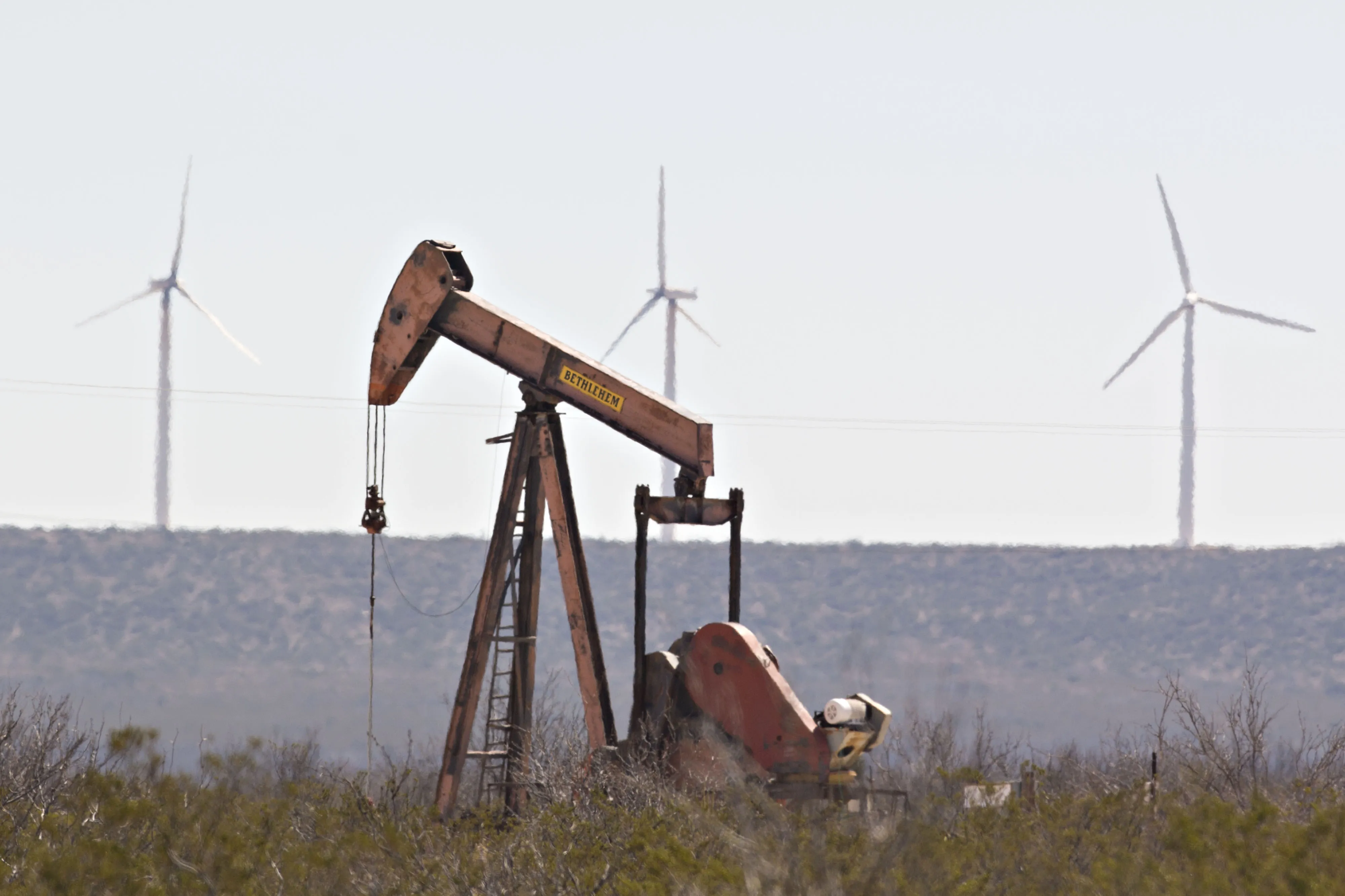 Wind turbines overlook a&nbsp;pumpjack operating&nbsp;on an oil well in the Permian Basin near Crane, Texas on March 2, 2018.