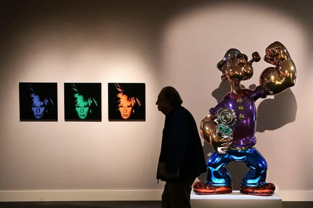 A prospective buyer browses gallery space featuring Andy Warhol's Six Self Portraits and Jeff Koons' Popeye.