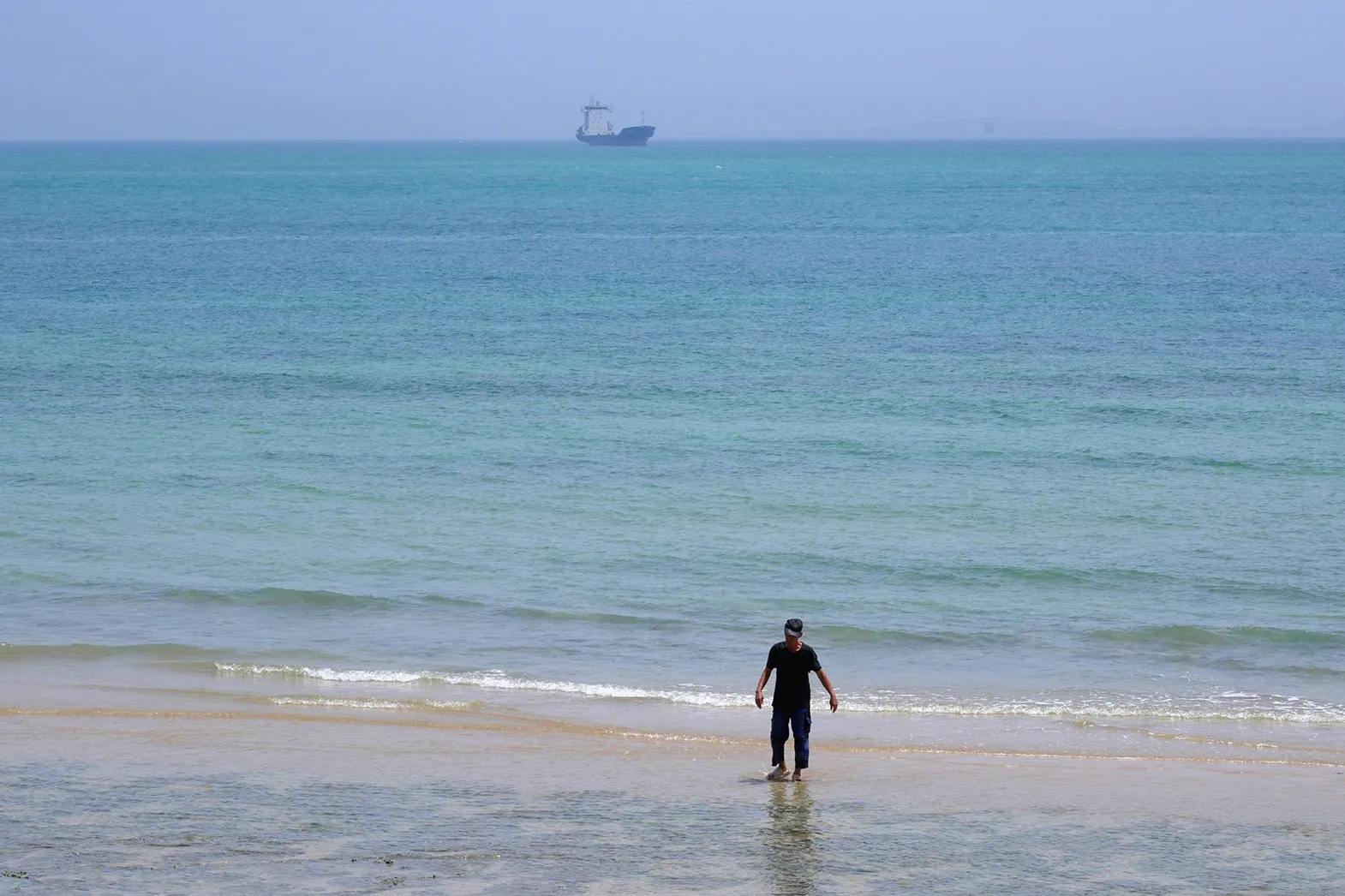 A man paddles on the beach as a ship is seen in the background on Qeshm Island, Iran in the Strait of Hormuz..