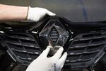 A worker attaches a Renault diamond badge to the front grille of an automobile.