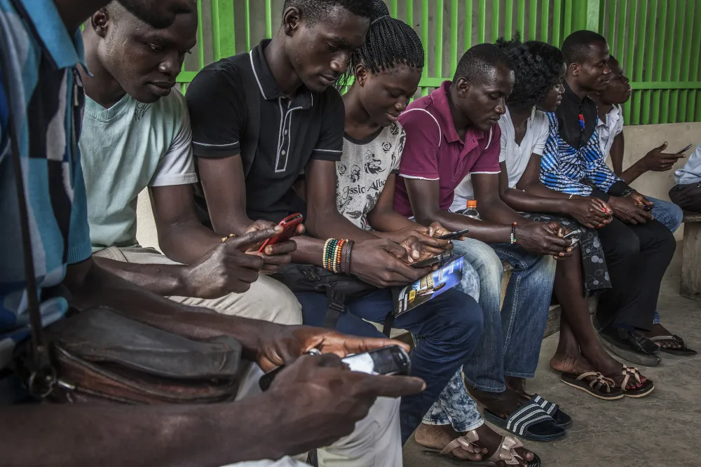 People&nbsp;use their mobile phones while waiting to board a ferry in Abidjan, Ivory Coast.
