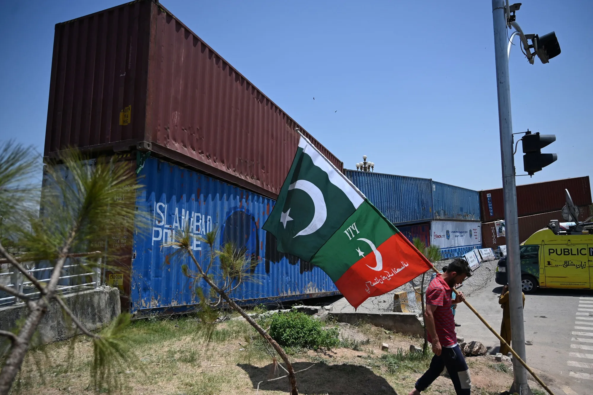 A supporter of Pakistan Tehreek-e-Insaf (PTI) party, carries flags next to containers stacked by the authorities to block the Red Zone ahead of the sit-in planned in Islamabad, Pakistan, on May 24.