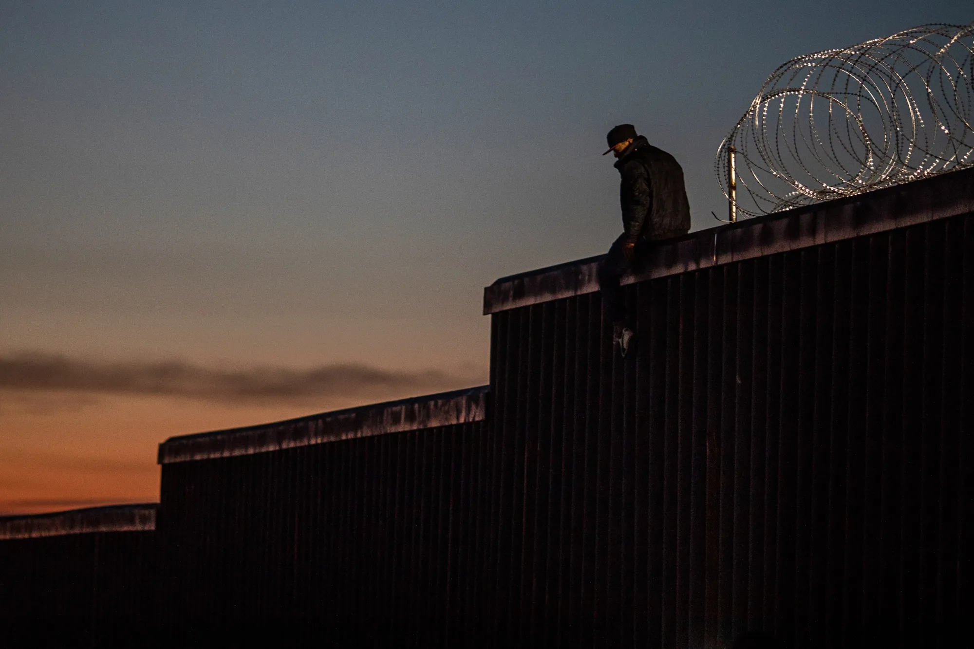 A man sits on top of a section of a U.S.-Mexico border wall at dusk in Tijuana, Mexico.