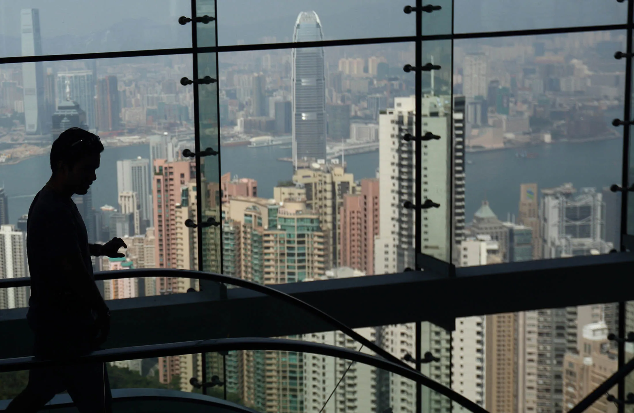 A visitor rides on an escalator at Victoria Peak as buildings stand in the distance in Hong Kong, China, on Sunday, Oct. 5, 2014. A week into Hong Kong demonstrations notable for their order and endurance, protesters came under an attack highlighting the fault lines of a city torn between commercial interests and a desire for greater democracy.

