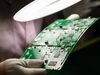 An employee in protective clothing inspects a circuit board.
