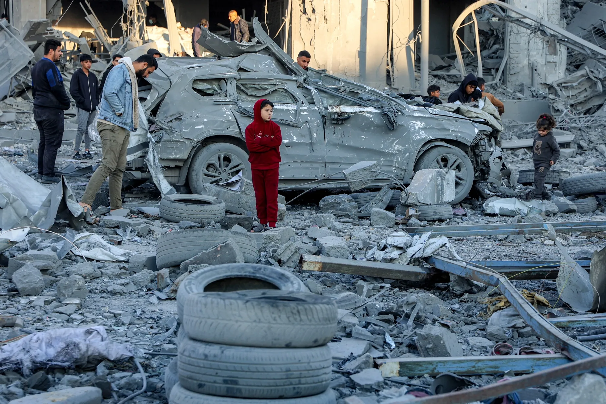 Men and children stand next to a destroyed car amidst debris and rubble from an&nbsp;Israeli bombardment&nbsp;in&nbsp;Gaza City, on Jan. 14.&nbsp;