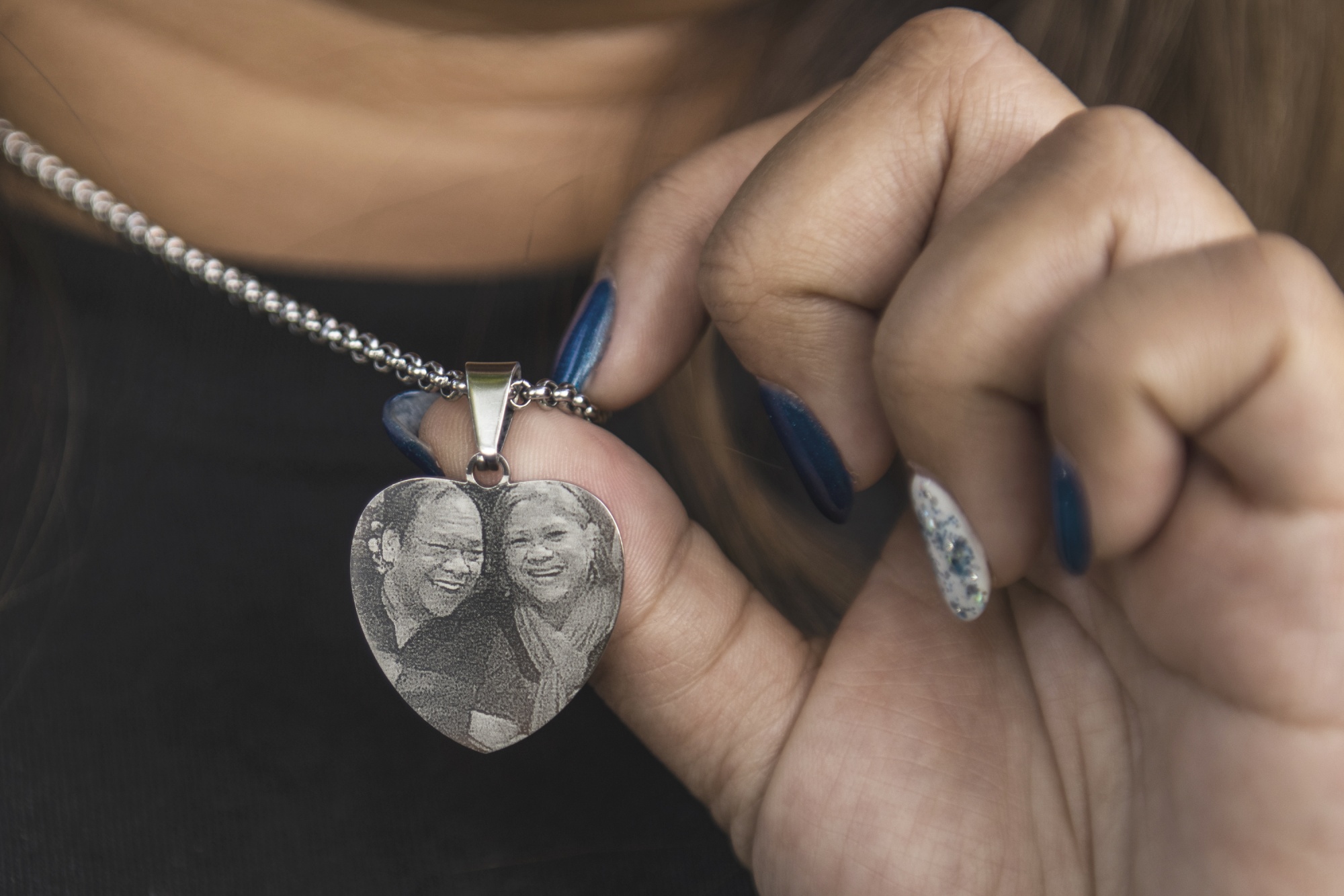Sheryl Pabatao holds a necklace with a photo of her parents Susana and Alfredo Pabatao who both died of COVID-19.