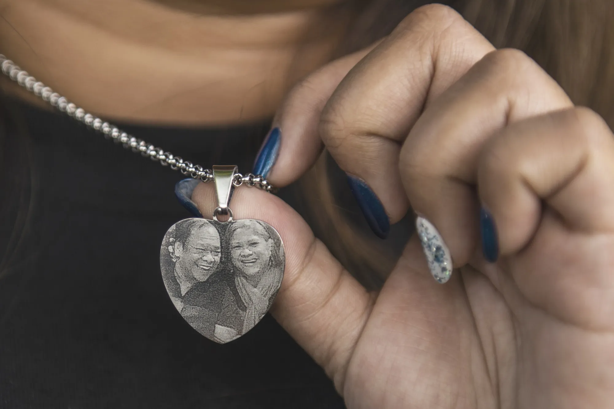 Sheryl Pabatao holds a necklace with a photo of her parents Susana and Alfredo Pabatao who both died of COVID-19.
