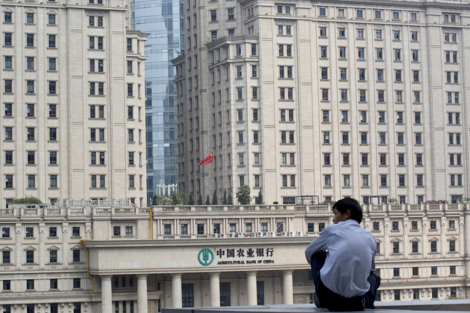 A man sits on a ledge in front of the Agricultural Bank of China Ltd. branch in Guangzhou.