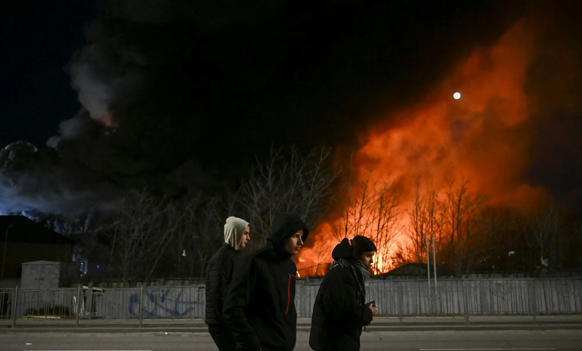 Youths walk past a burning warehouse after shelling in Kyiv on March 17.&nbsp;