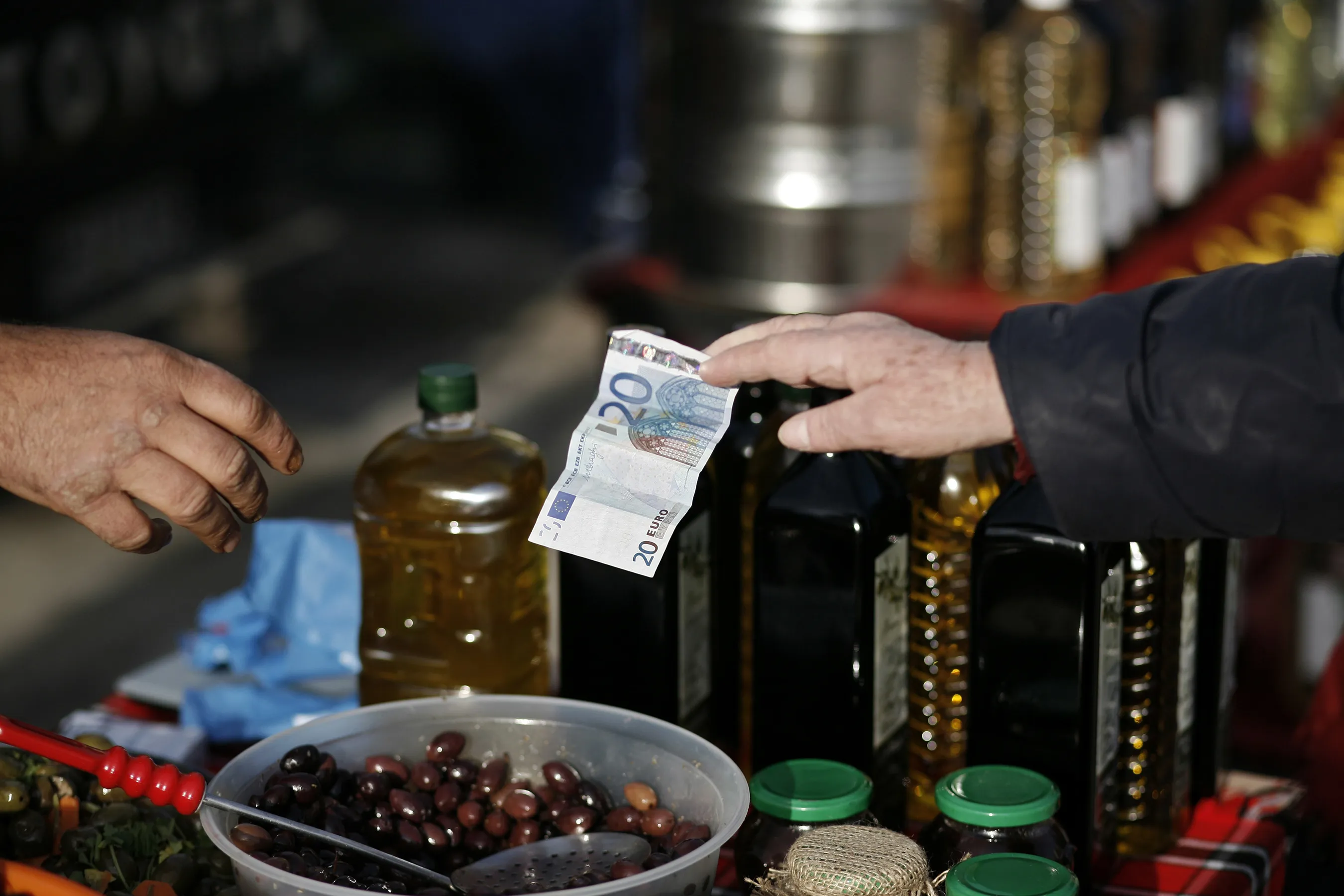 A customer uses a 20 euro banknote to pay for olives at a farmer's market in Thessaloniki.