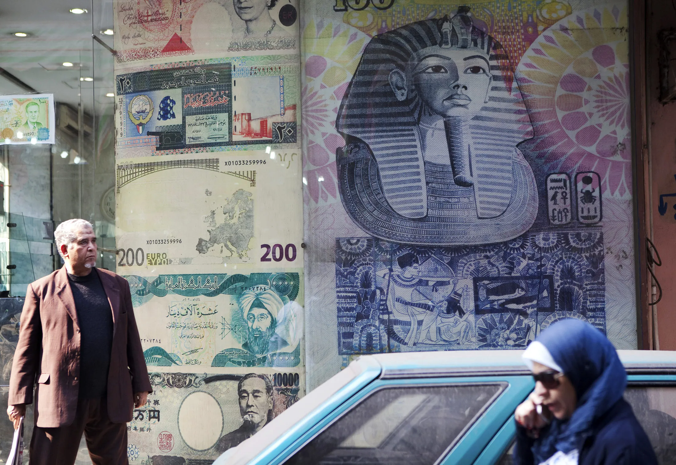 A woman, right, uses her mobile phone as she passes a currency exchange store in Cairo, Egypt.

