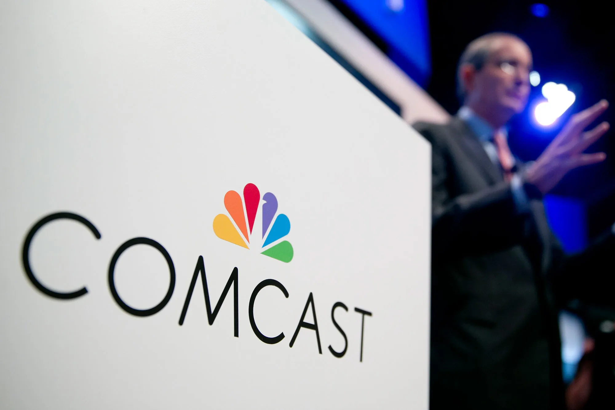 The Comcast Corp. logo is seen as Brian Roberts, chairman and chief executive officer of Comcast Corp., right, speaks during a news conference at the National Cable and Telecommunications Association (NCTA) Cable Show in Washington, D.C., U.S., on Tuesday, June 11, 2013.
