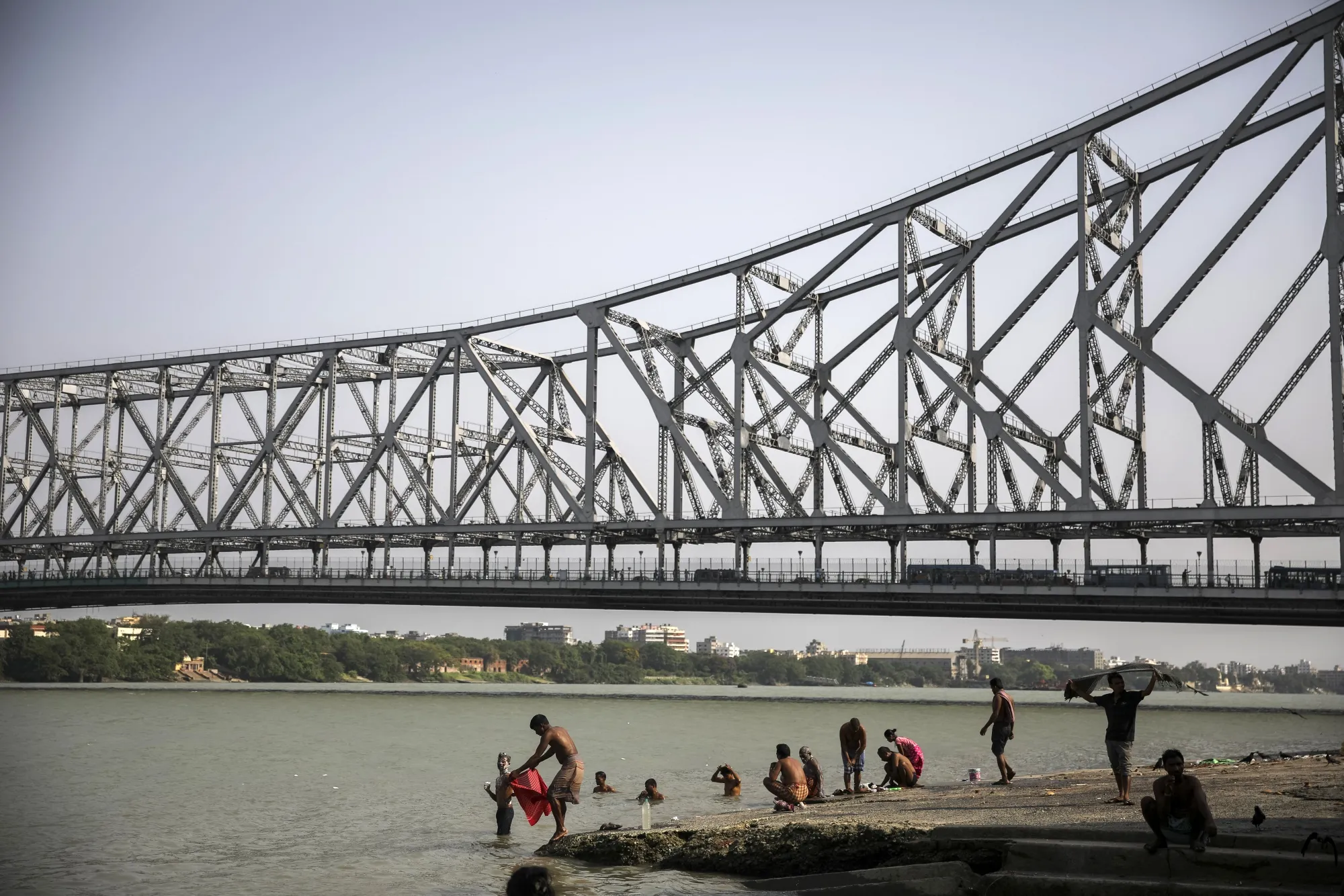 People bathe on the banks of the Hooghly River near the Howrah Bridge in Kolkata, India.