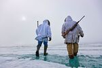 Inupiaq Eskimo hunters carry a rifle and walking stick while walking over the shore ice along the Chukchi Sea, Barrow, Alaska.

