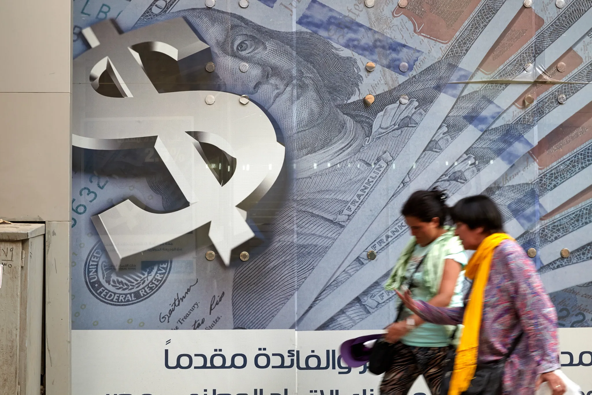 Pedestrians walk past an advertisement displaying a large dollar sign and U.S. dollar banknotes outside a bank in Cairo.