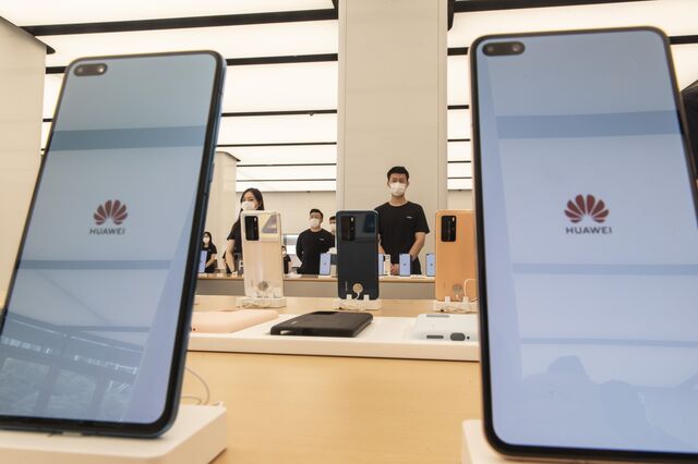 Huawei employees wearing protective masks stand behind a display of smartphones.