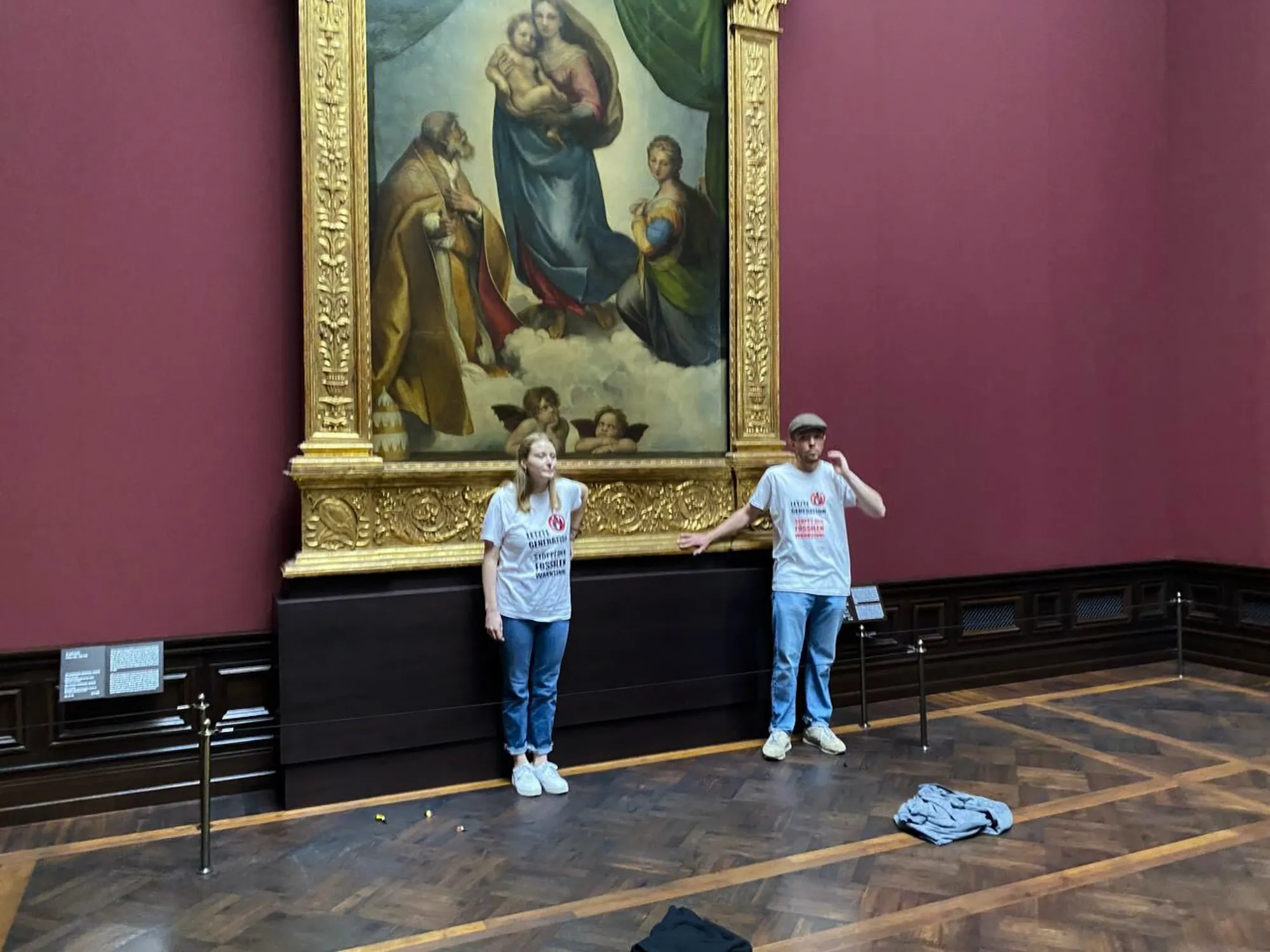In this photo provided by the climate activist group 'Letzte Generation', Last Generation, shows activist glued themselves to the frame of the painting 'Sistine Madonna' by Raffael at the Gemaeldegalerie Museum in Dresden, Germany, Tuesday, Aug. 23, 2022. (Letzte Generation via AP)
