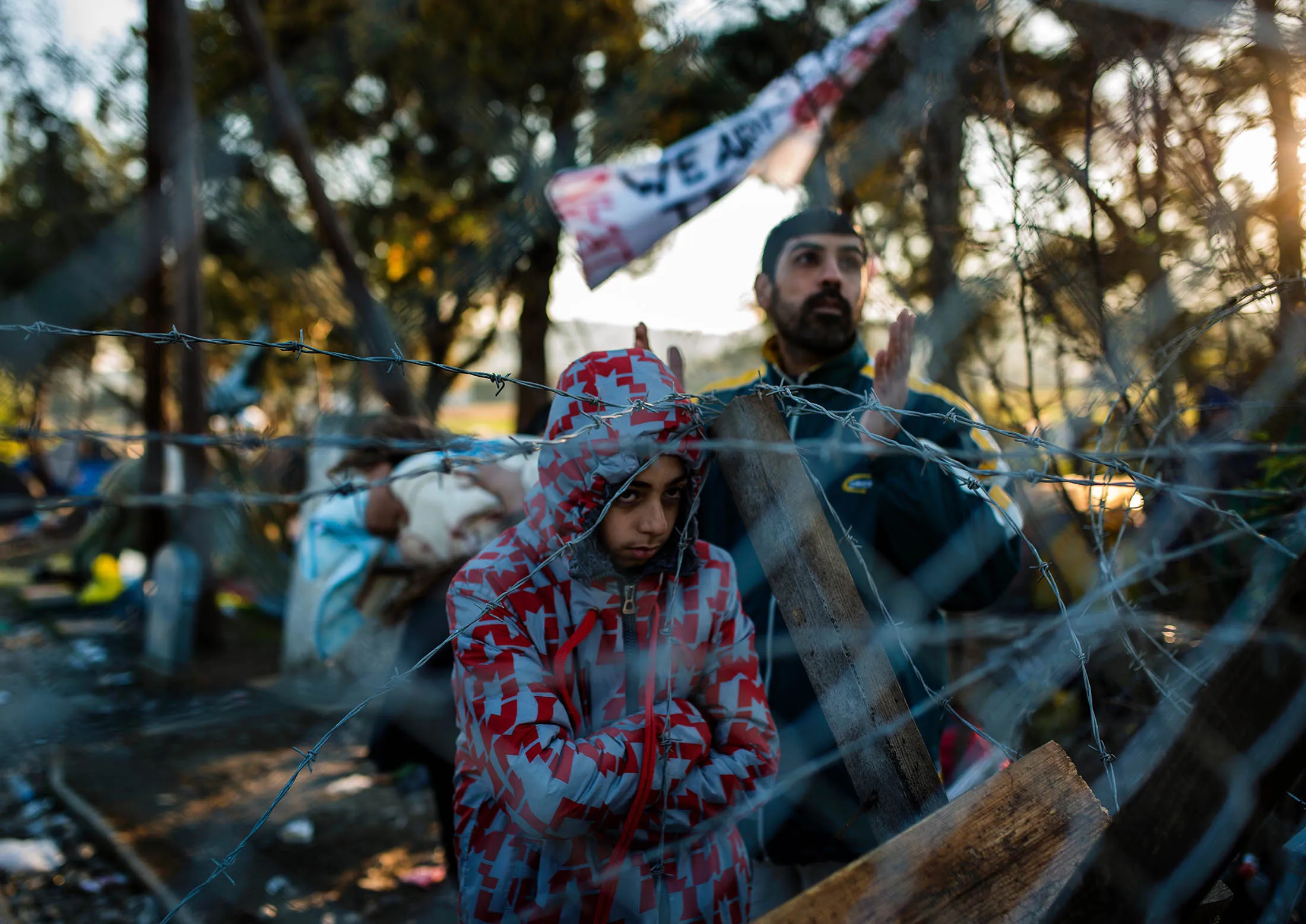Refugees stand behind a wire fence as they wait to cross the Greek-Macedonian border.
