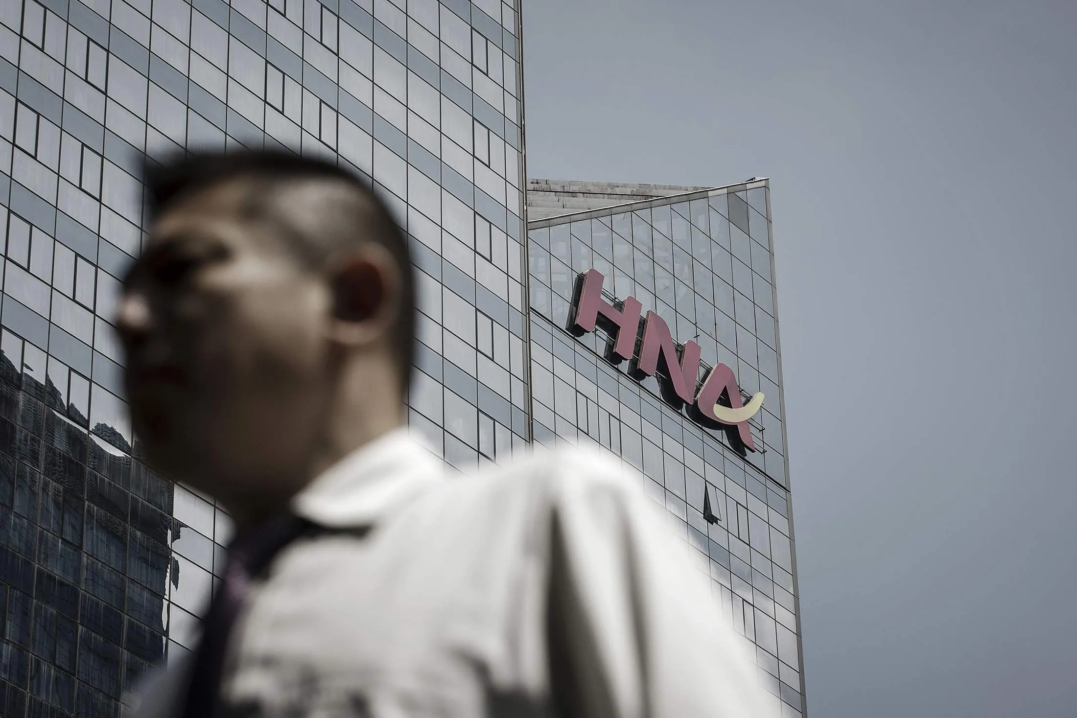 A pedestrian walks past the HNA Group Co. building in Beijing.
