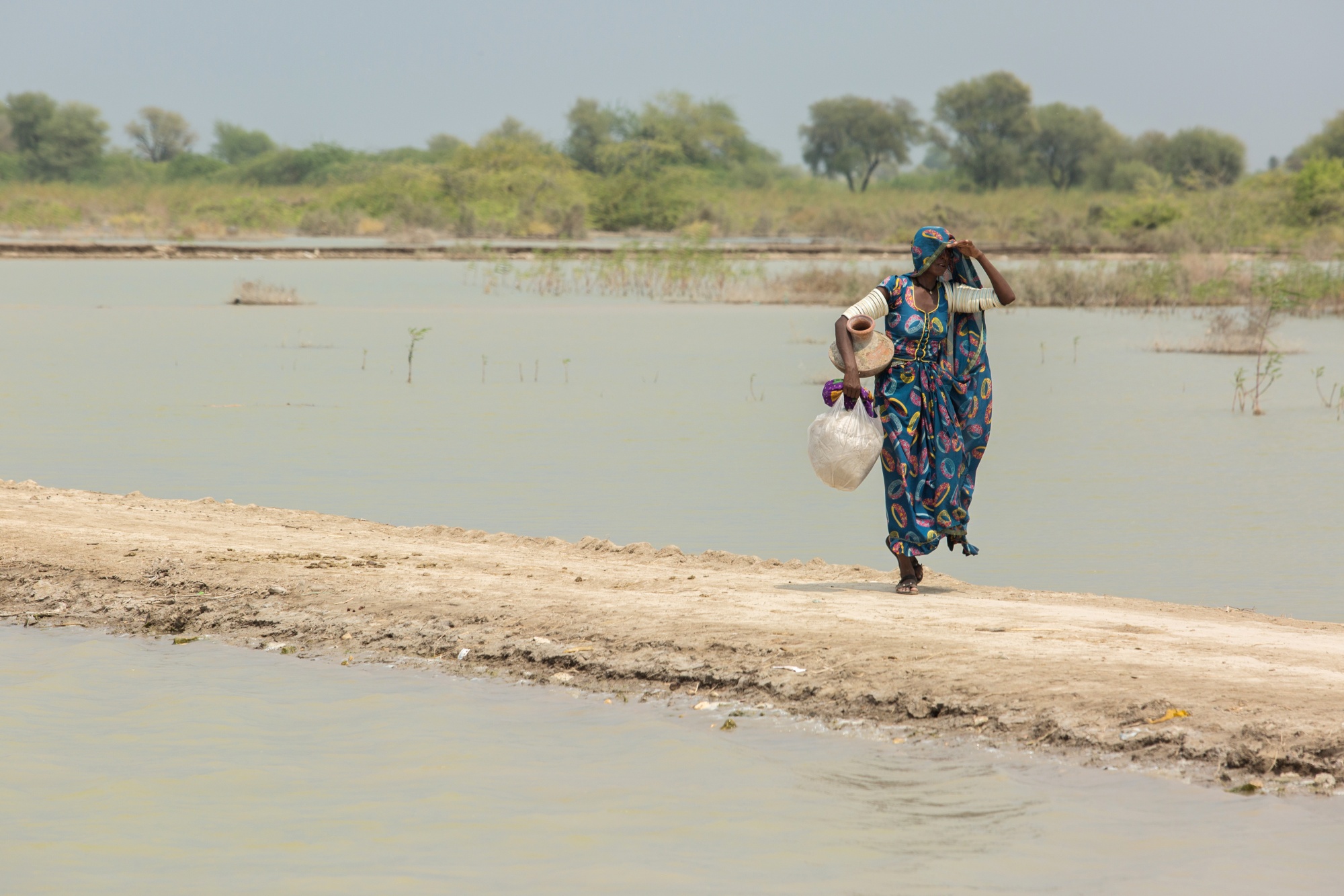 A woman carries a pot to fill with drinking water through a flooded area of Umerkot district in Sindh province, Pakistan, Sept. 10, 2022.&nbsp;