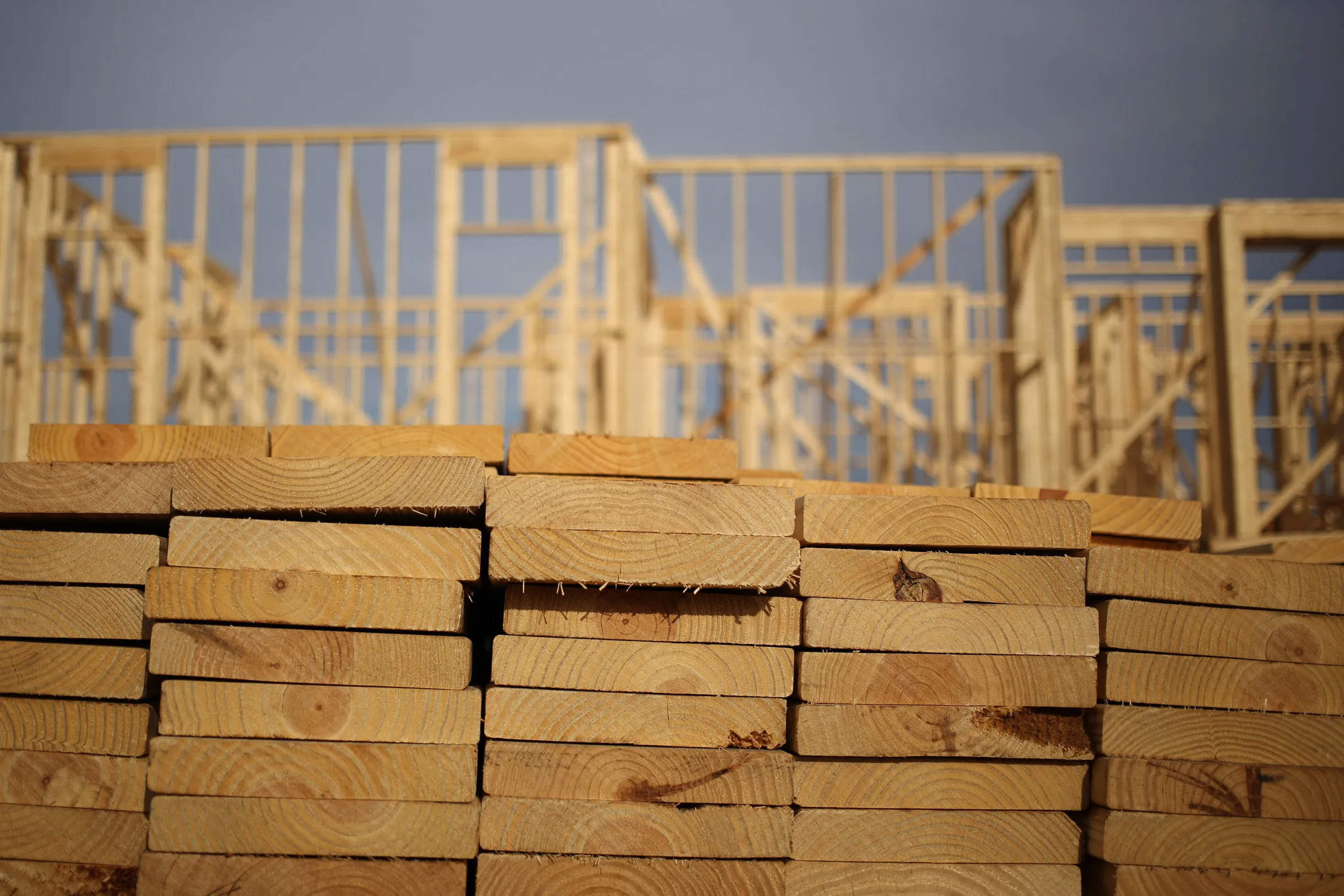 Lumber sits stacked in front of wooden framing during the construction of residential housing
