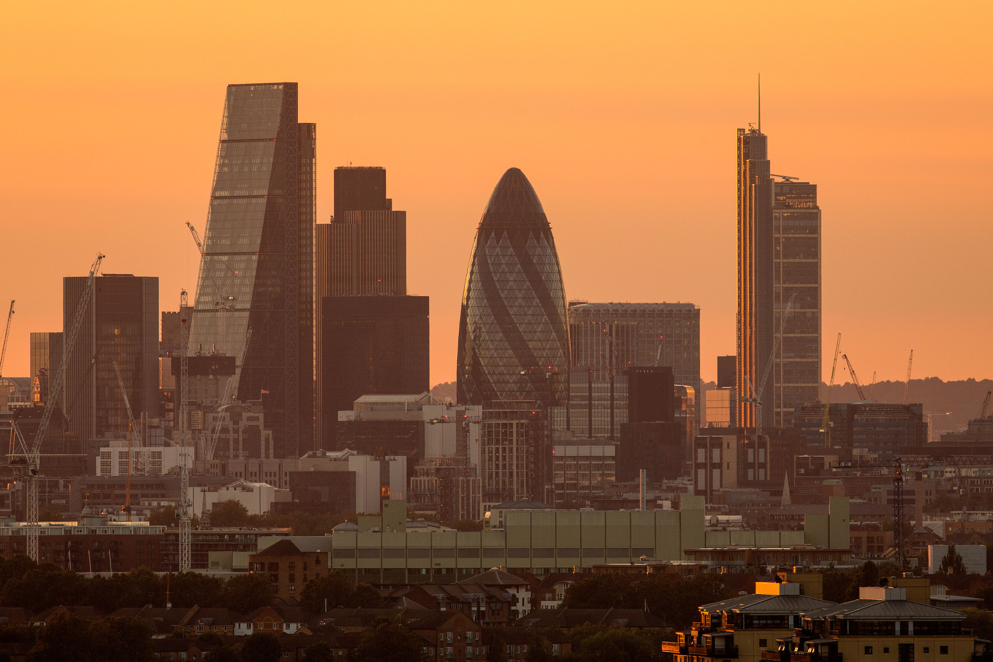 The sun sets on the horizon beyond skyscrapers including The Leadenhall Building, also known as the 'Cheesegrater,' left, Tower 42, second left, 30 St Mary Axe also known as 'the Gherkin,' center, and The Heron Tower, right, in the City of London, U.K.