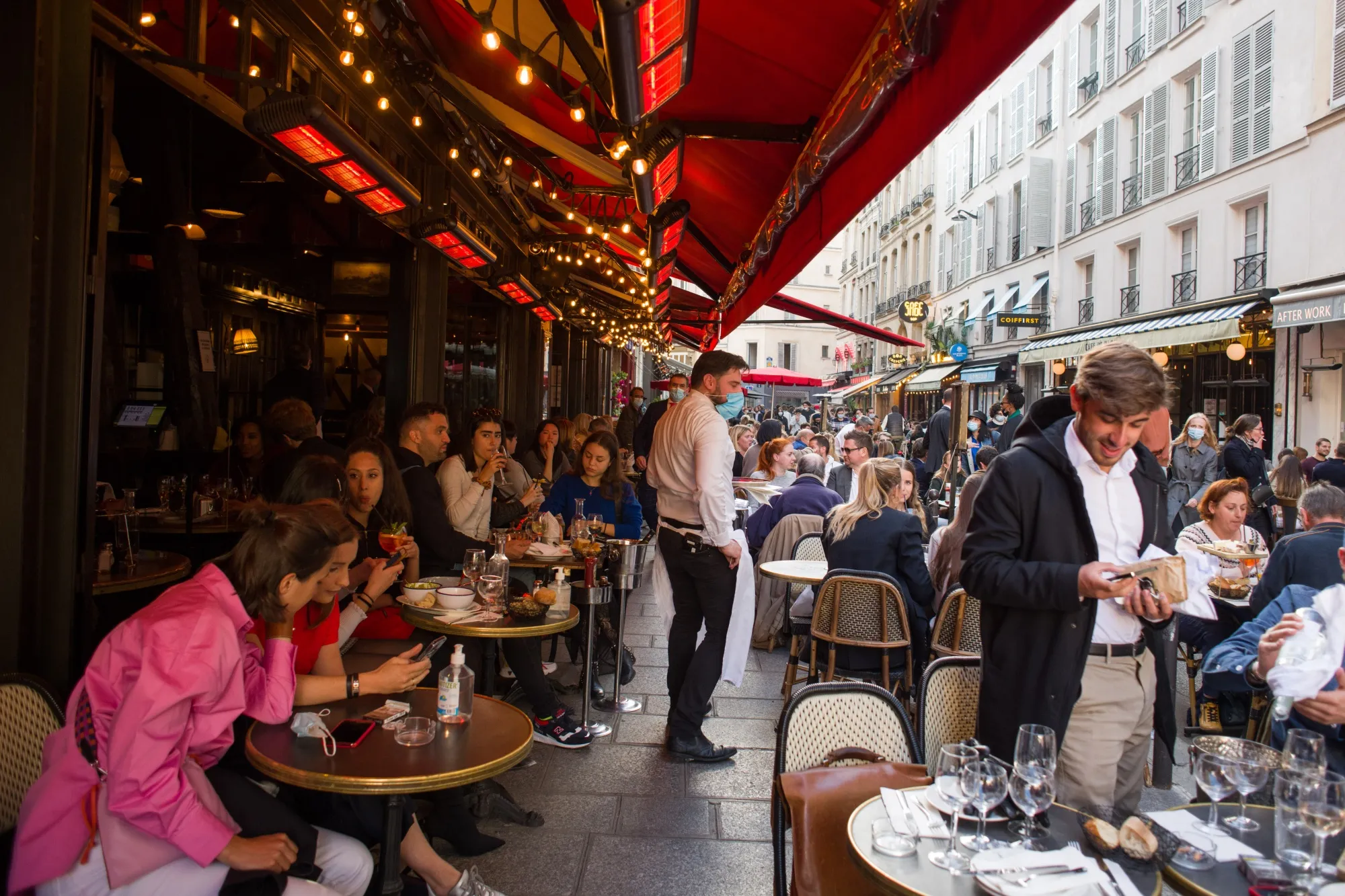 A waiter wearing a protective mask serves customers at a cafe in Paris.