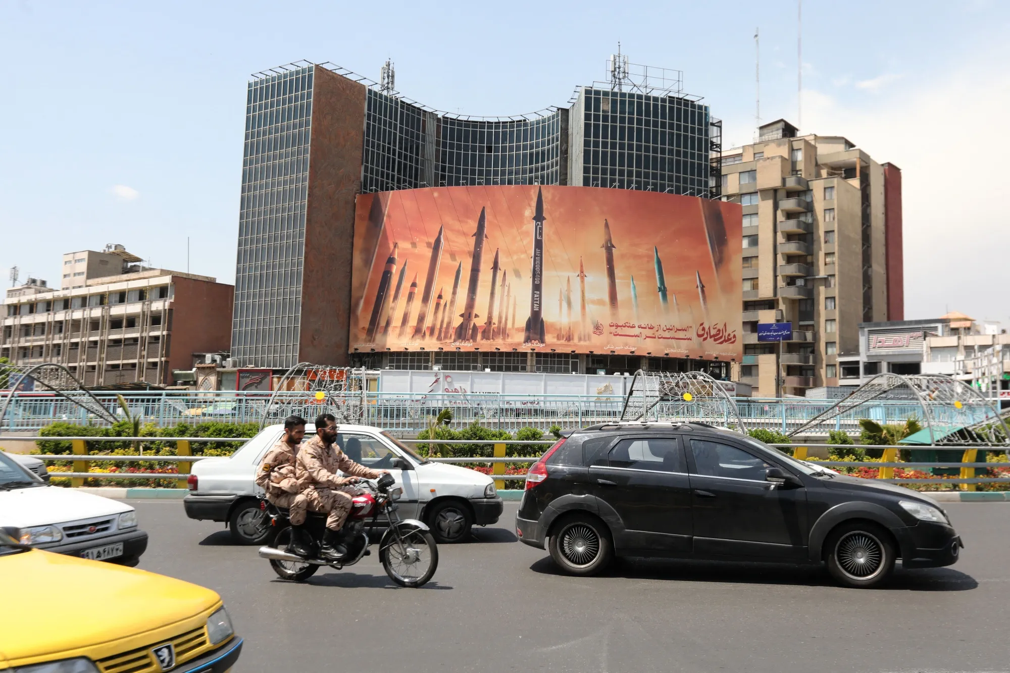 Motorists drive their vehicles past a billboard depicting Iranian missiles in Tehran.
