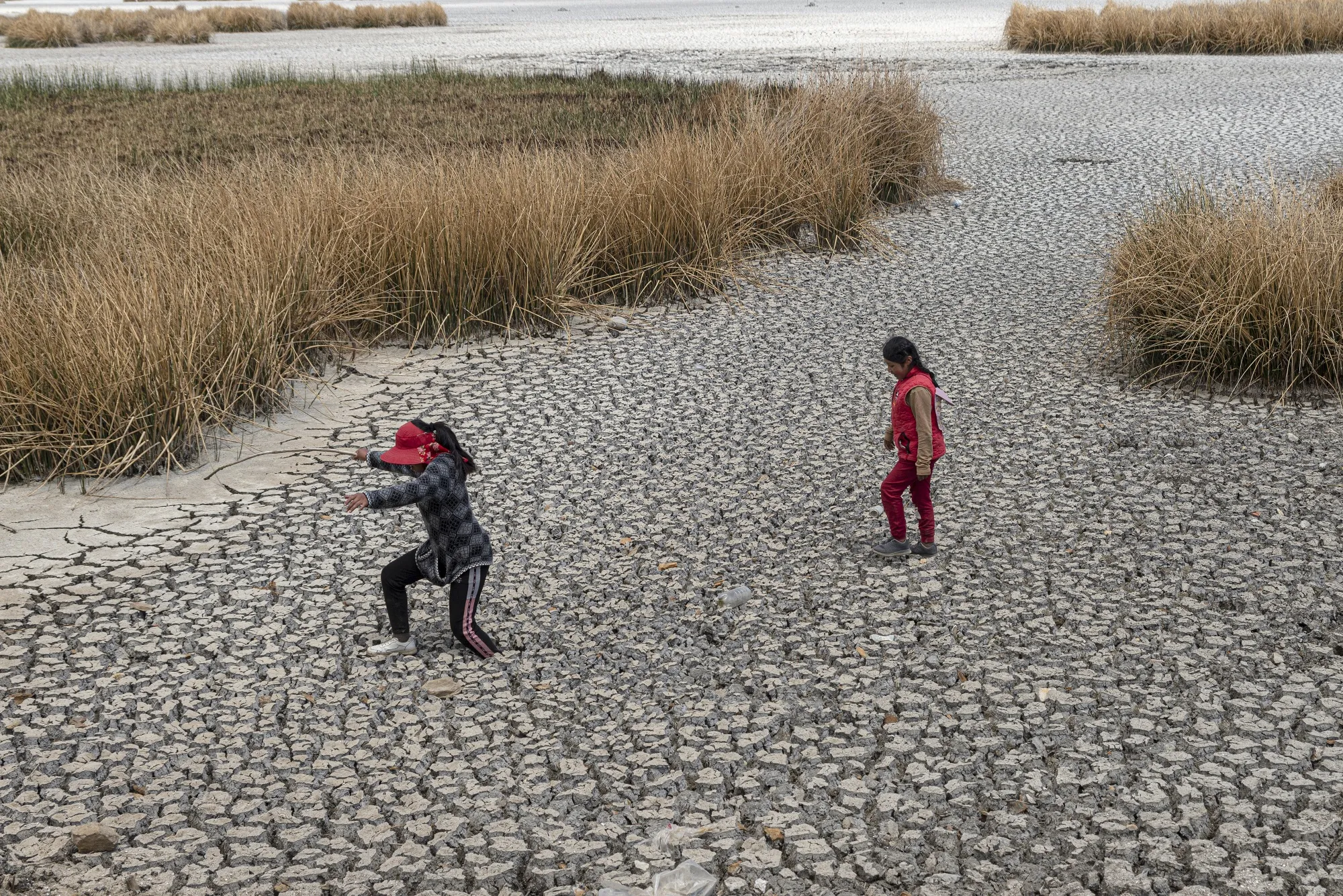 Children walk over muddy ground during drought conditions at Lake Titicaca in Huarina, Bolivia.