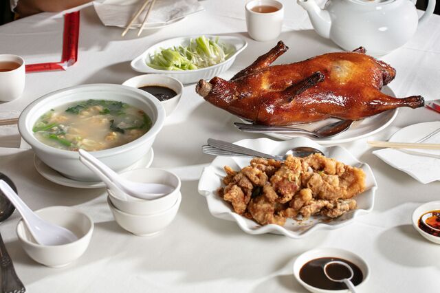 A roasted pig on a white table, accompanied by bowl of wonton soup, empty bowls and soup spoons, chopsticks and chicken on plate.