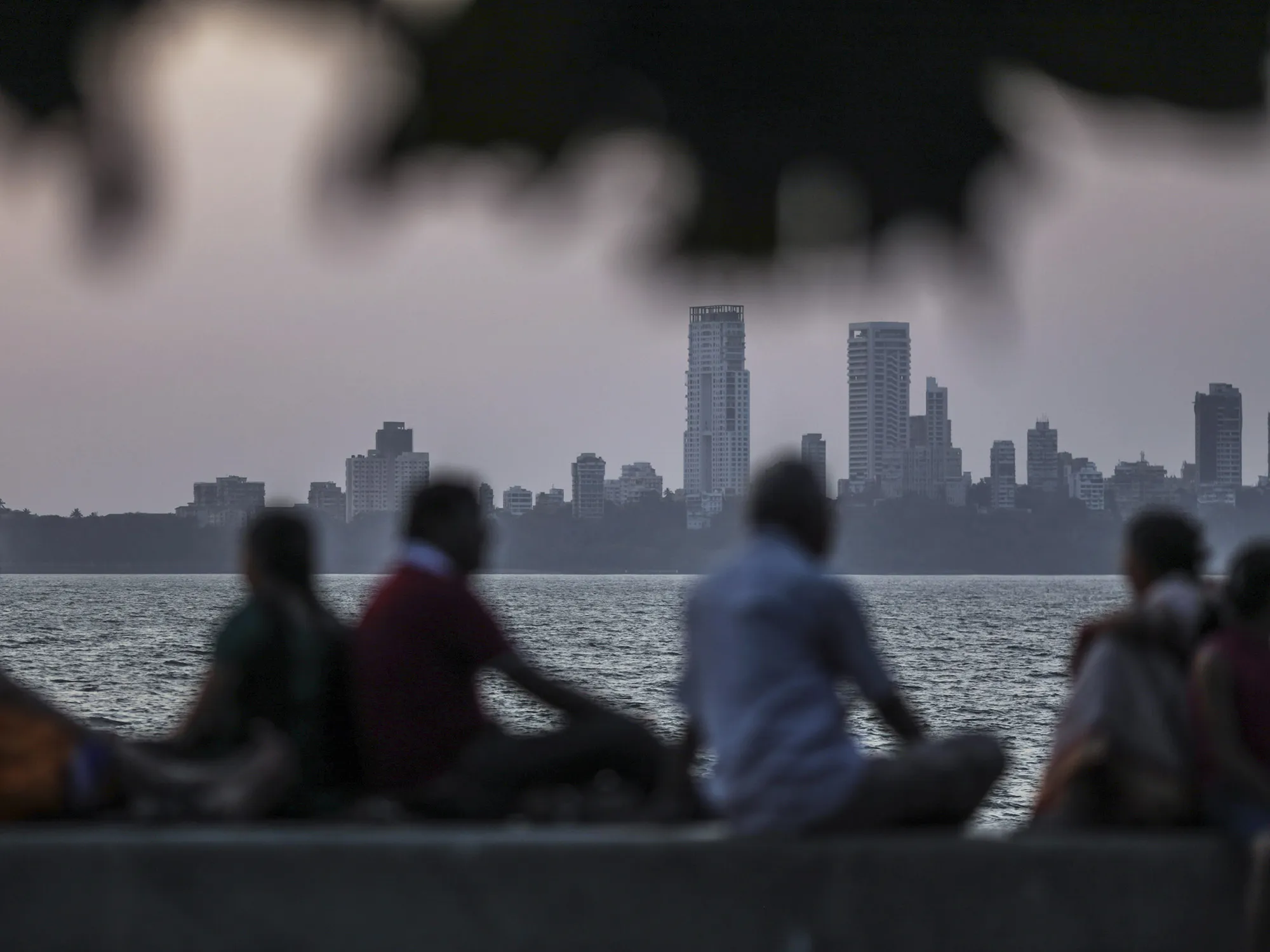 People sit on the waterfront as commercial and residential buildings stand in the background in the Nariman Point area of Mumbai.