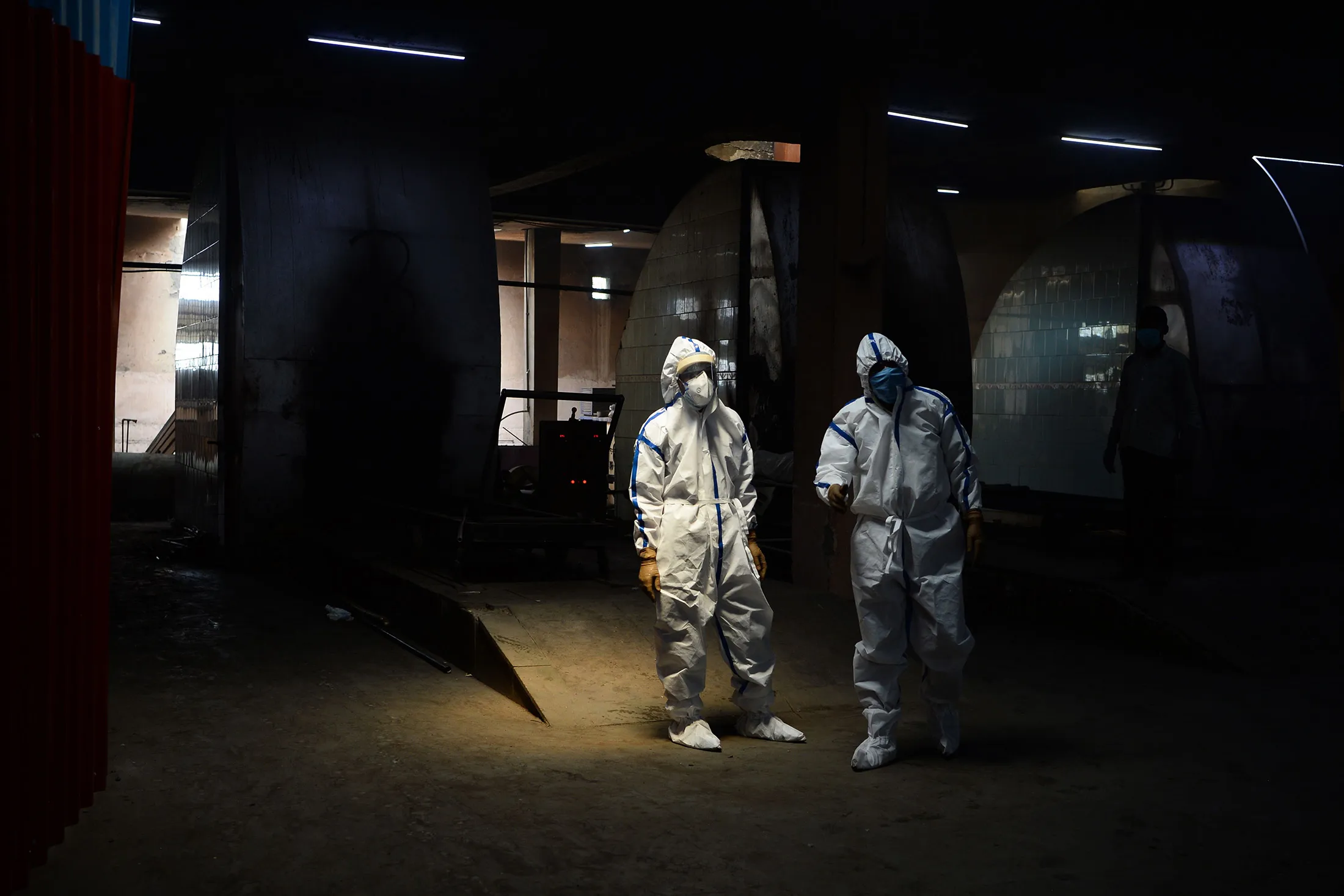Workers wearing Personal Protective Equipment (PPE) next to cremation furnaces at the Nigambodh Ghat cremation ground in New Delhi in 2020.
