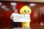 Mr Li in yellow costume receives 219 million yuan cash cheque from Guangxi Welfare Lottery Center’s party chief Lan Ting.