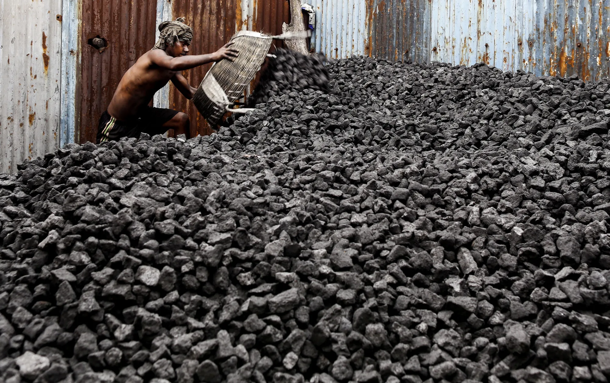 A worker unloads a basket of coal onto a coal heap at a coal wholesale market in Mumbai, India.
