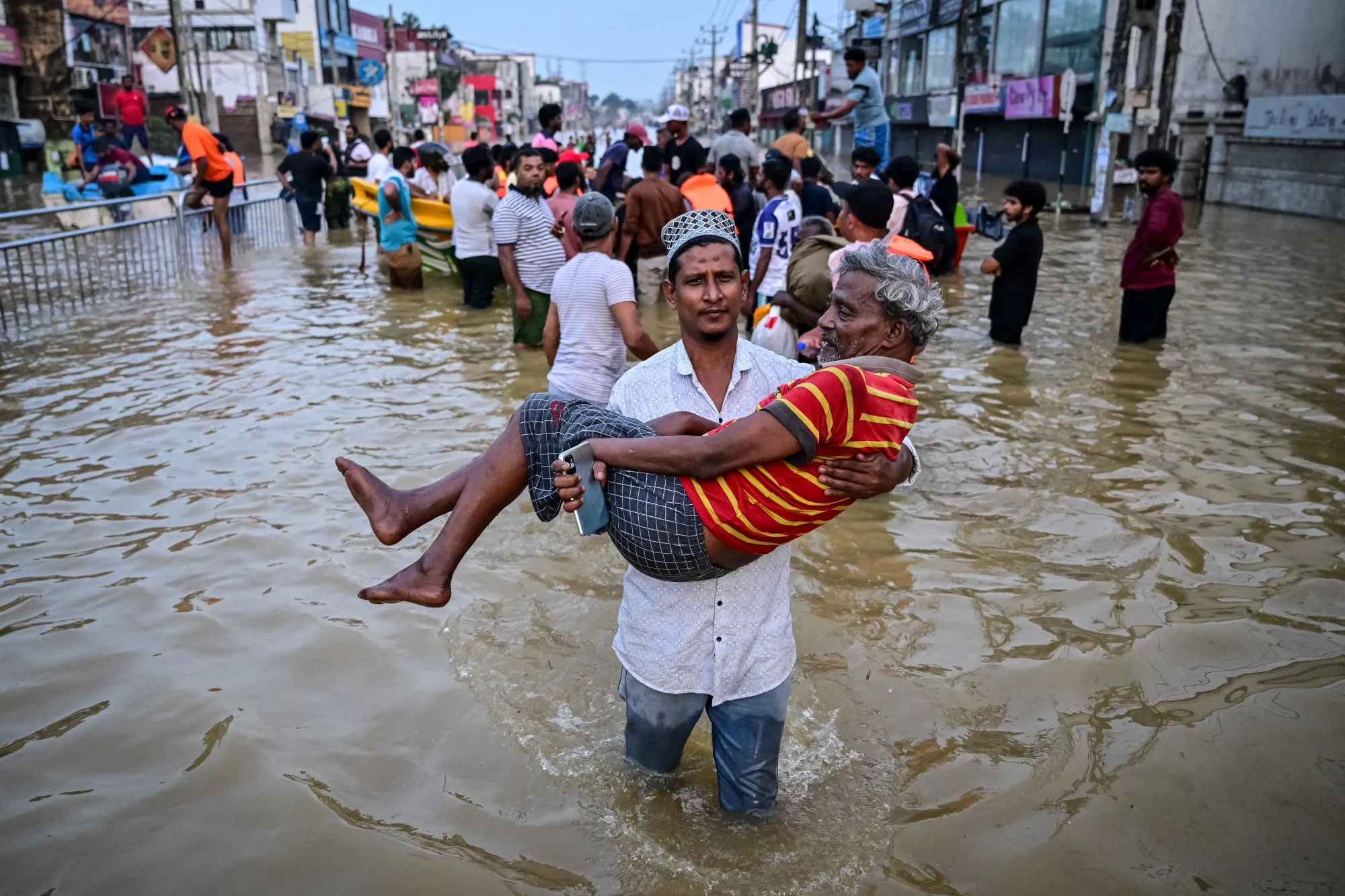 A youth carries an elderly man as they wade through a flooded street in Colombo on Nov. 30.