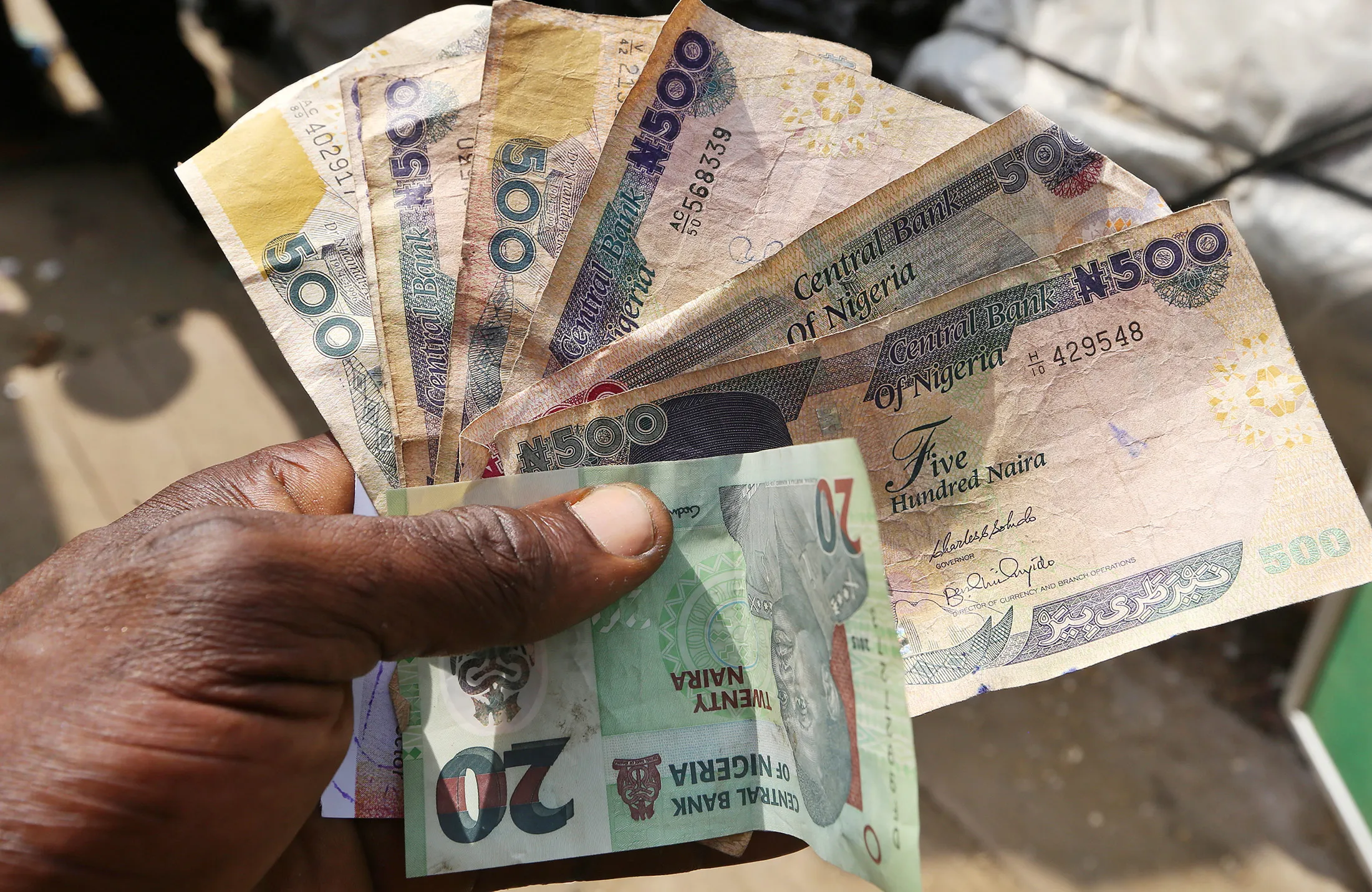 A trader holds 20 and 500 denomination naira banknotes at the Swali market in Yenagoa, Nigeria, on Thursday, Jan. 14, 2016.
