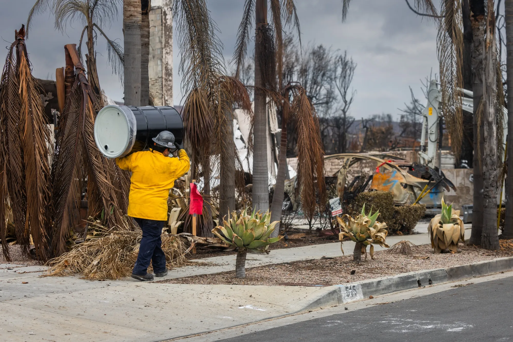 An cleanup worker carries a barrel to hold lithium-ion batteries that will be removed from an electric vehicle&nbsp;in the Pacific Palisades.