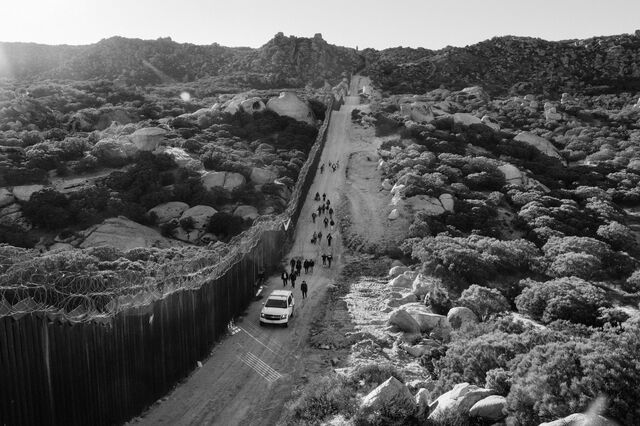 Asylum seekers follow a US Custom and Border protection vehicle along the Mexico-US border fence near Boulevard. 