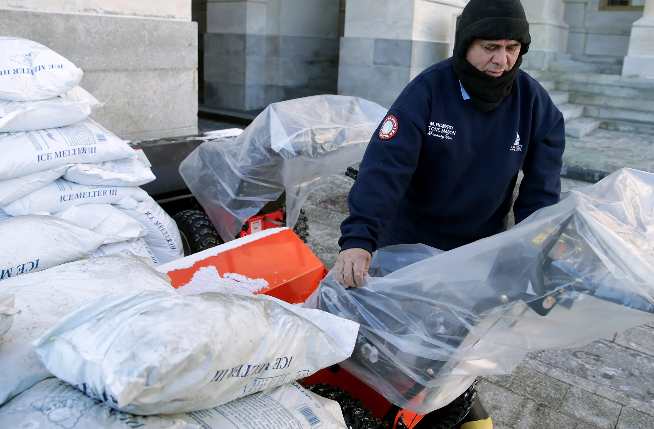Surrounded by bags of ice-melting salt, a worker covers snow sweepers in plastic bags in preparation for a coming winter storm outside the U.S. Capitol in Washington, DC., on Jan. 21
