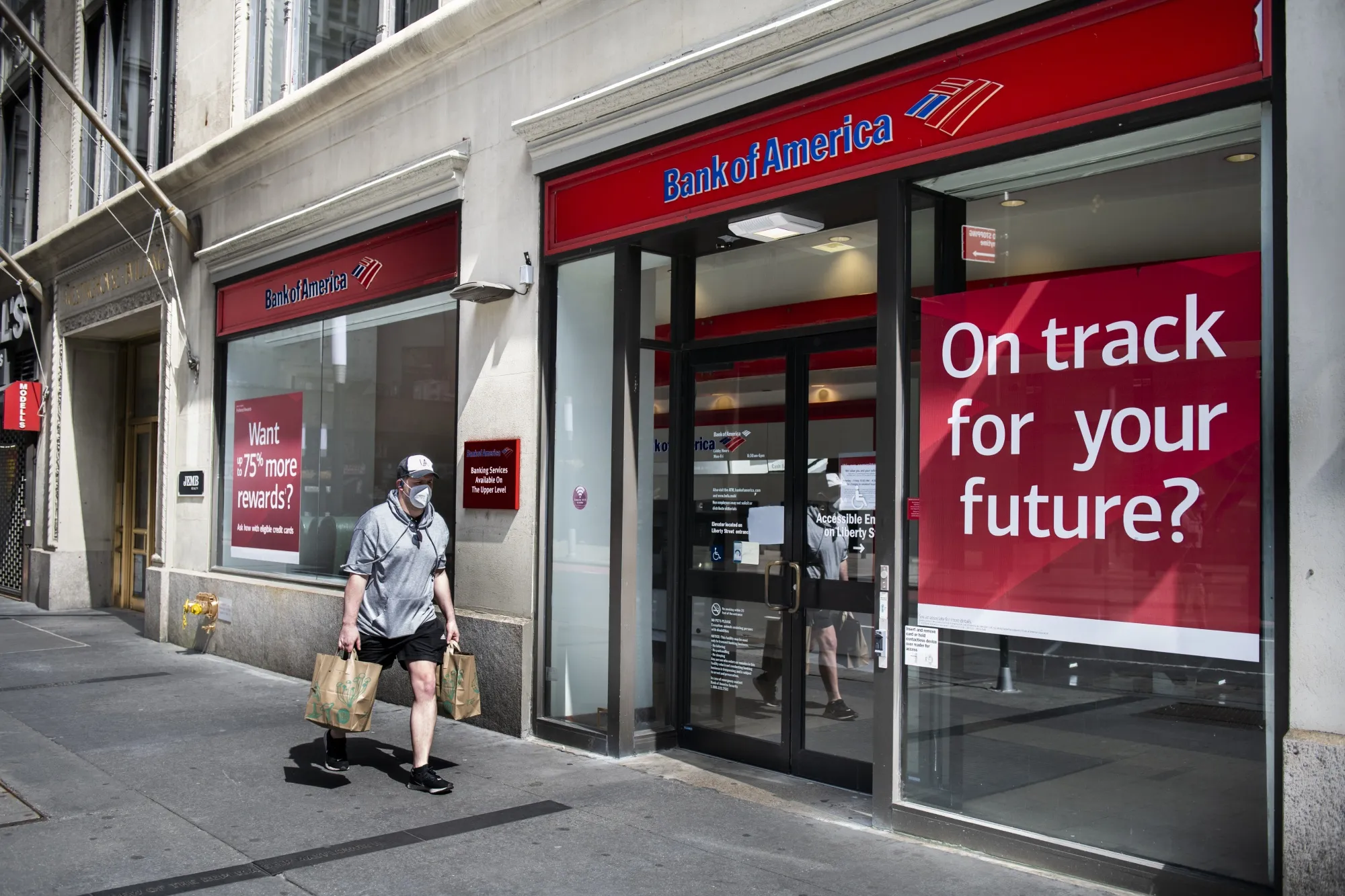 A pedestrian wearing a protective mask passes a Bank of America Corp. branch in New York on April 11.&nbsp;
