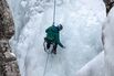 An ice climber screws in an ice screw anchor as he rappels down a 160' high ice wall in the Ouray Ice Park