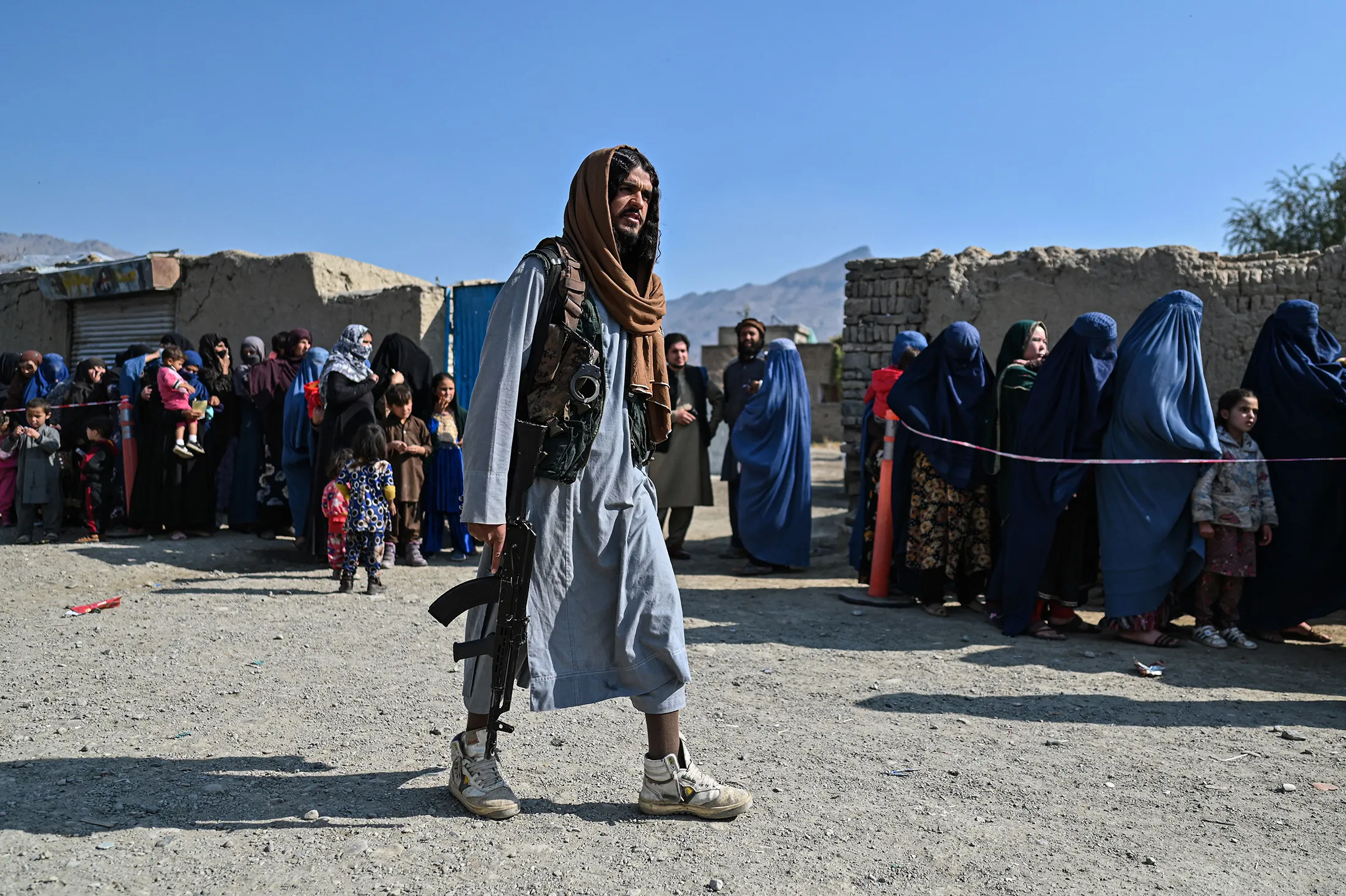 A Taliban fighter passes women waiting in line during a World Food Program food distribution near Kabul on Nov. 6.