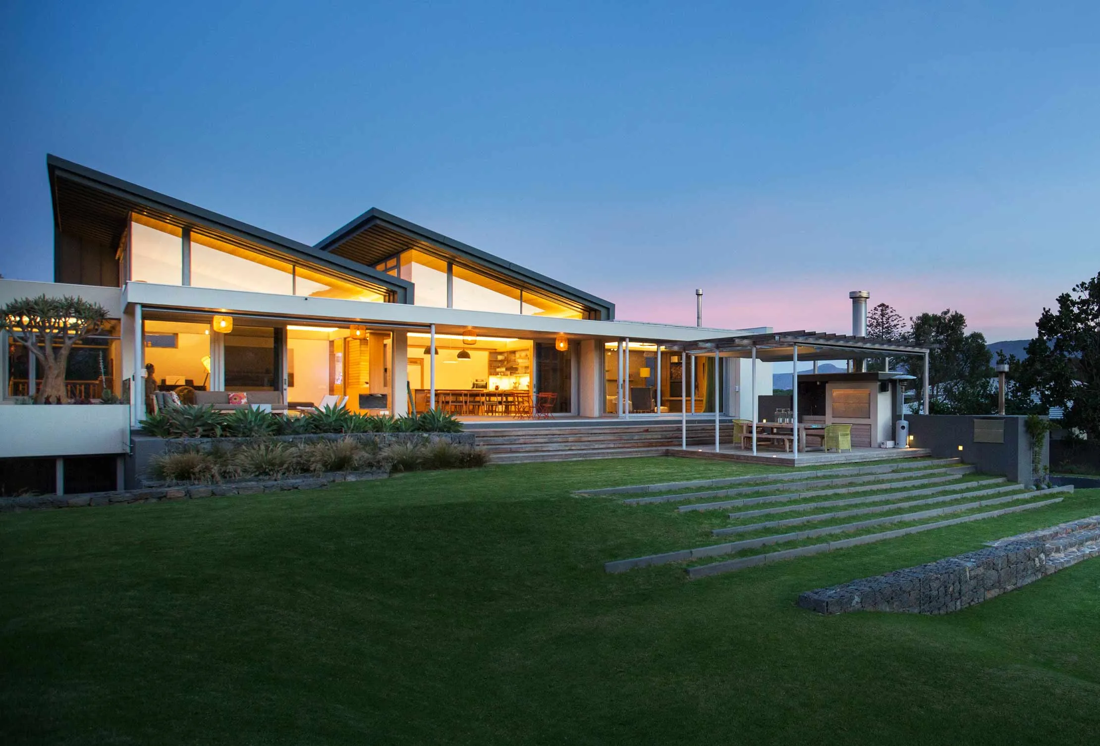 Illuminated modern house beyond yard and swimming pool at night
