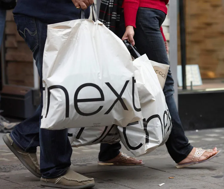 Shoppers carry Next branded bags from a Next Plc store in London.
