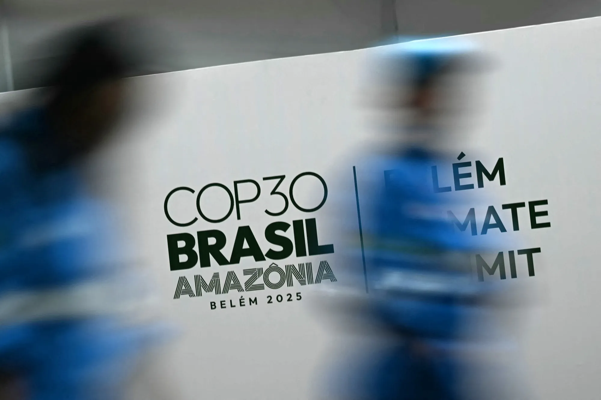 Workers walk past a banner with the COP30 UN Climate Change Conference logo inside the Hangar Convention and Exhibition Center in Belem, Para State, Brazil on November 5, 2025.&nbsp;