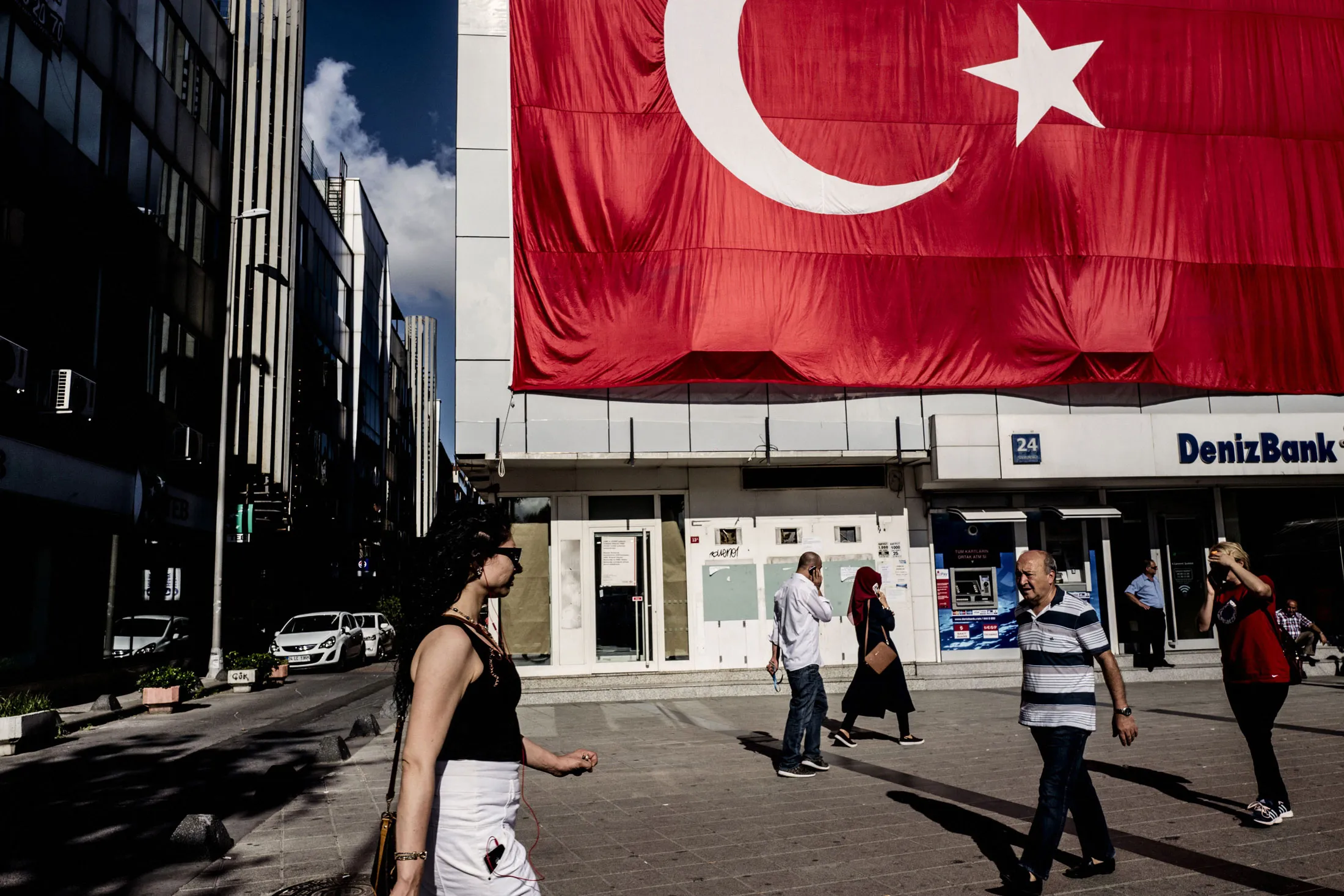 Pedestrians pass a giant Turkish national flag hanging above a DenizBank AS bank branch in Istanbul
