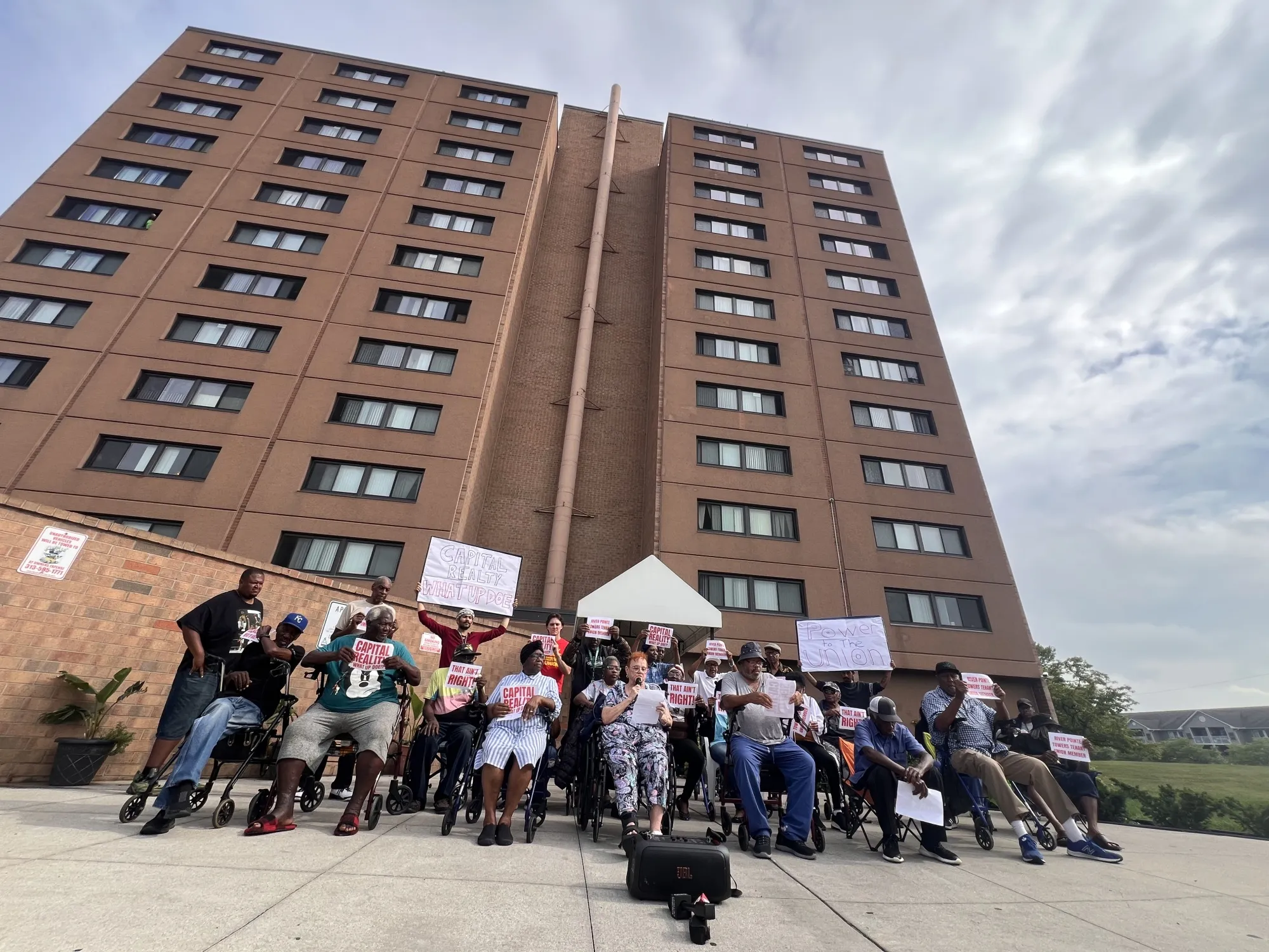 Senior residents of the&nbsp;River Pointe Tower apartments in Detroit hold signs with the name of the building’s New York owner, Capital Realty Group.