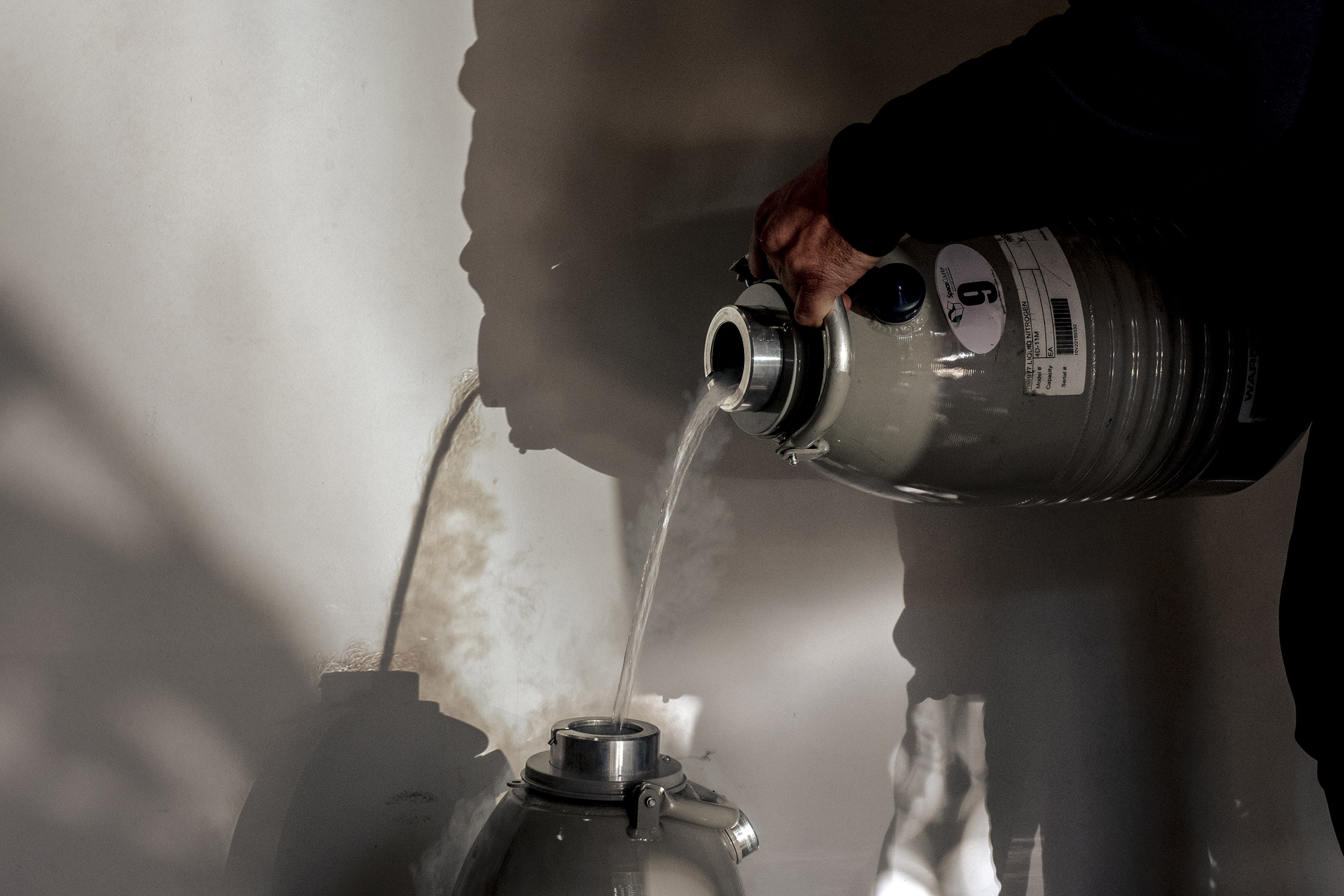 Clear liquid from a green medical canister is poured into another. 